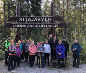 Retkeilijät ryhmäkuvassa Ritajärven luonnonsuojelualueen kyltin edessä syksyllä 2021.